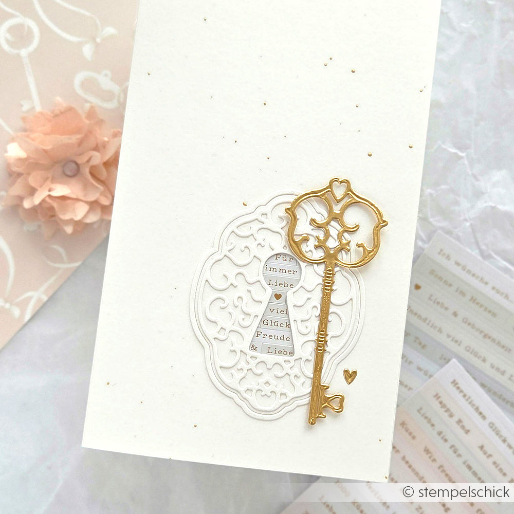 Elegante Karte mit einem goldenen Schlüssel und einem filigranen weißen Ausschnitt, hergestellt mit dem Alexandra Renke Motivstanze Schlüsselloch-Ornament DieCut System, plus deutschem Text auf weißem strukturiertem Designpapier.