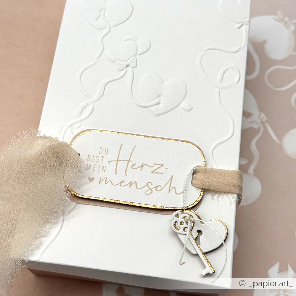 Weiße Geschenkschachtel von Alexandra Renke, geprägt mit Motivstanze Schlüssellochherzen, veredelt mit beigem Band, Schlüsselanhänger und dem Text "Du bist mein Herzmensch". Ideal zum Verschenken Ihrer liebsten Designpapiere.