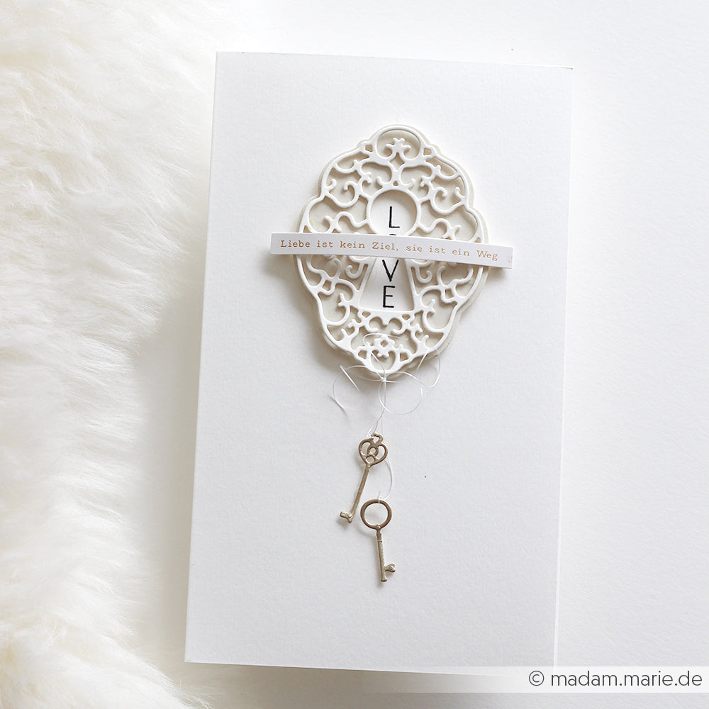 Elegante weiße Karte von Alexandra Renke mit vertikalem Schriftzug "LOVE", kunstvollem DieCut Systeme-Ausschnitt, deutschem Zitat und zwei silbernen Schlüsseln - gefertigt auf feinen Designpapieren mit Motivstanze Schlüssellochherzen.