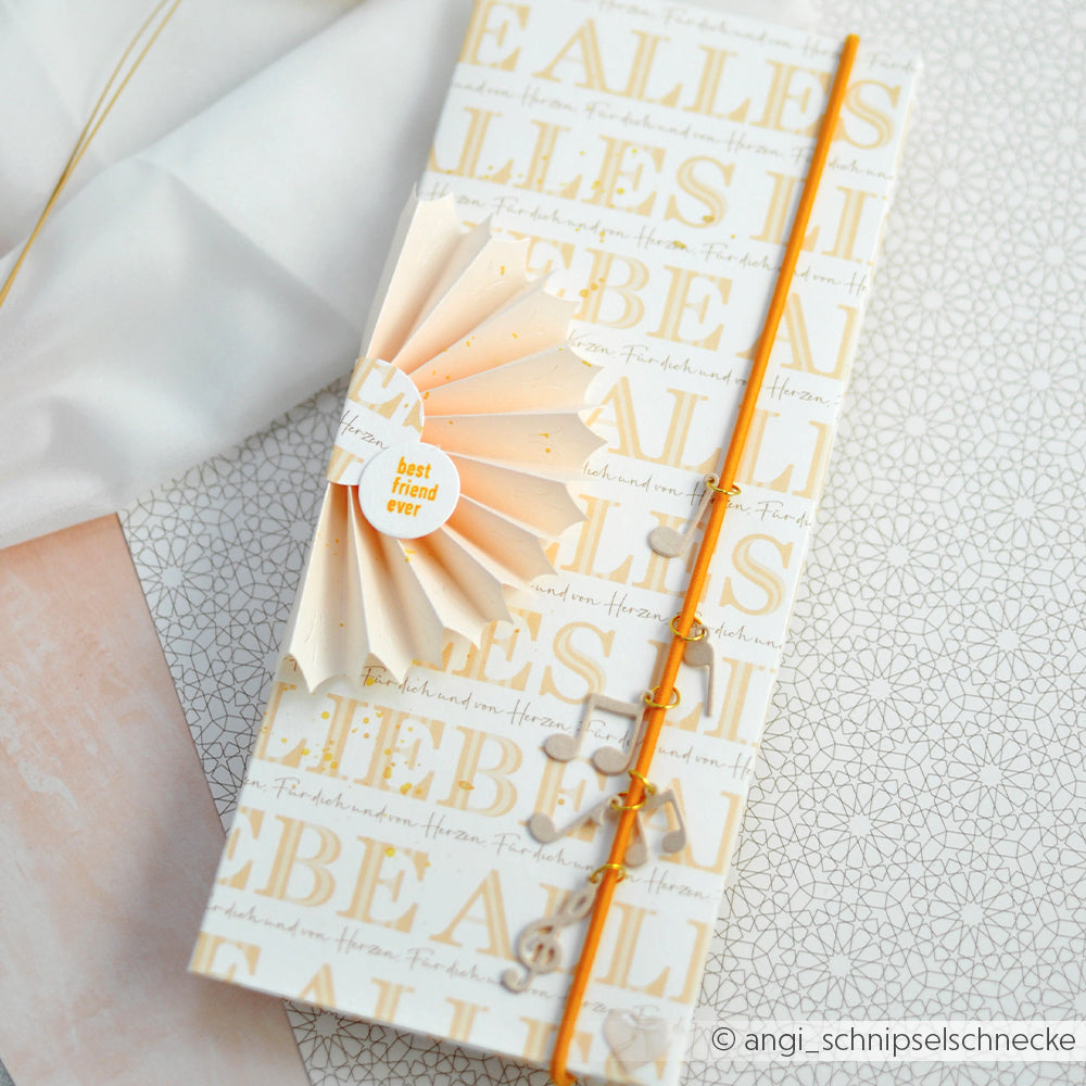 Eine handgefertigte Karte von Alexandra Renke mit goldener Schrift, einer Papierrosette, vertikal gewickelter orangefarbener Schnur und einzigartigen Akzenten von Designpapieren.