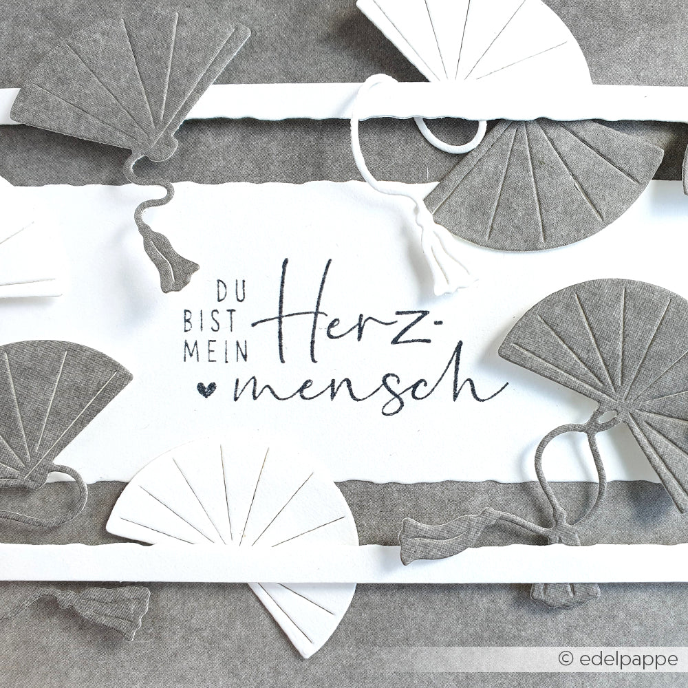 Graue und weiße Papierfächer, die mit Alexandra Renkes Motivstanze Fächer Trio und eleganten Designpapieren gestaltet wurden, umrahmen deutsche Kalligrafie auf weißem Papier.