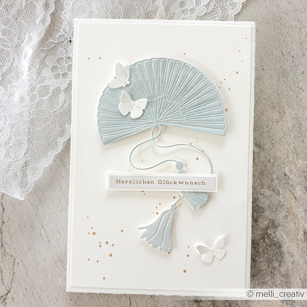Handgefertigte Karte von Alexandra Renke mit einem blauen Fächer (Motivstanze Großer Fächer), weißen Schmetterlingen, Quasten und "Herzlichen Glückwunsch" auf weißen Designpapieren 200g.