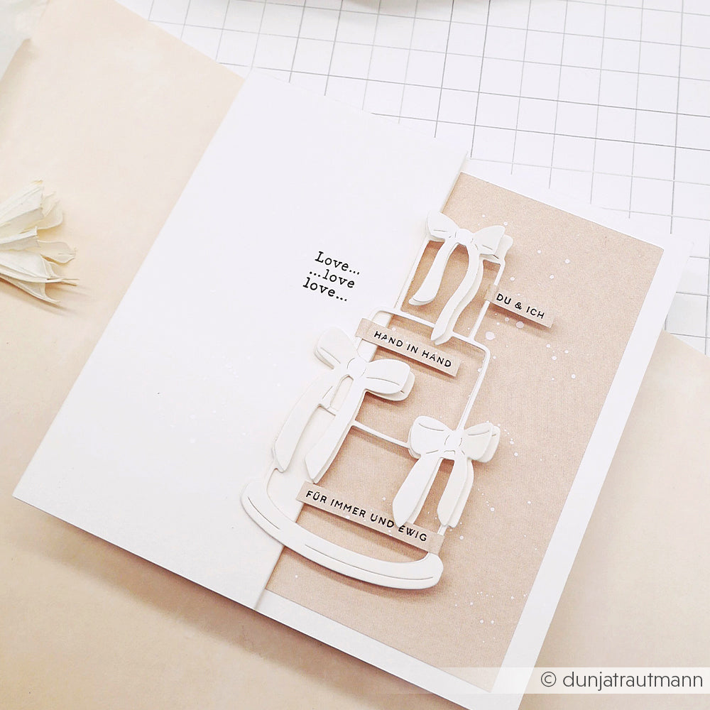 Eine handgefertigte Hochzeitskarte von Alexandra Renke mit einer geschichteten Outline Torte und deutschen Liebessprüchen auf beige, gefertigt mit hochwertiger Motivstanze für ein elegantes Finish.
