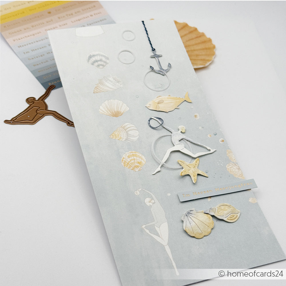 Handgefertigte Karte mit Motiven aus der Meereswelt – Muscheln, Fische, Anker – und einer ausgestanzten Ballerina, die mit der „Motivstanze“ und den „Figuren-Trio-Stanzen“ von Alexandra Renke gestaltet wurde; alles elegant auf einem hellen Hintergrund angeordnet.
