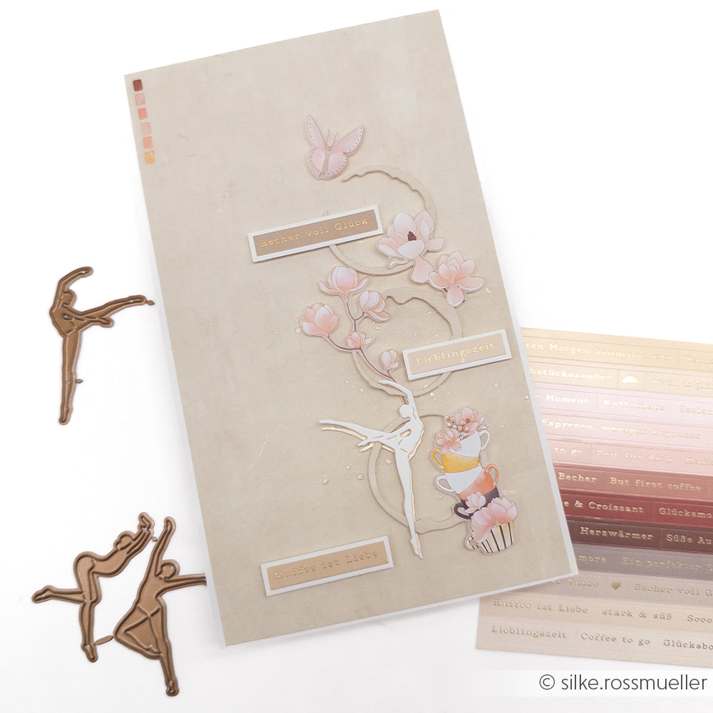 Eine beige Scrapbook-Seite mit Blumen-, Ballerina- und Schmetterlingsaufklebern sowie Ballerina-Ausschnitten aus Metall – perfekt abgestimmt auf die Designpapiere von Alexandra Renke für Ihre kreativen Projekte.