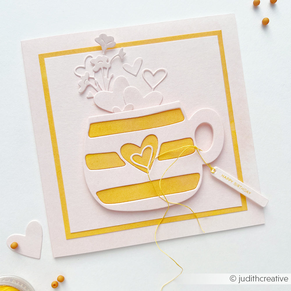 Handgefertigte Geburtstagskarte mit einer gelb-weiß gestreiften Tasse, aus Designpapier geformten Herzchen und einem kleinen „Happy Birthday“-Anhänger. Akzente setzt die Motivstanze „Große Herztasse“ aus unserer Stanzsysteme-Kollektion.