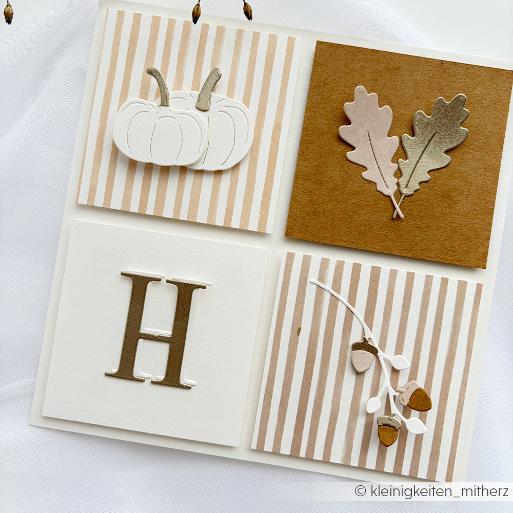 Quadratische Karte aus Designpapieren mit einem Kürbis, der mit der Motivstanze „Kürbis“ ausgestanzt wurde, zwei Eichenblättern, dem Buchstaben H und Eicheln auf gestreiftem und einfarbigem Hintergrund.