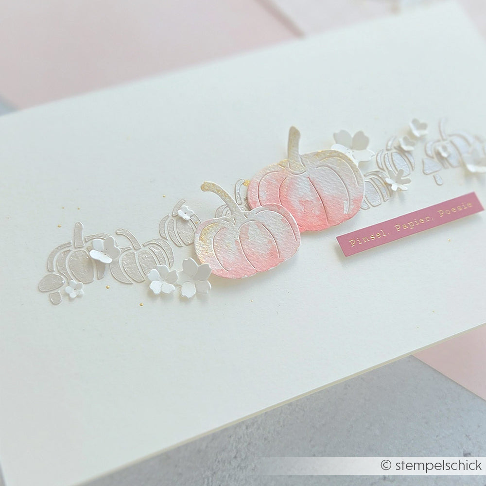 Eine handgefertigte Karte mit rosa Aquarell-Kürbissen und zarten weißen Blüten auf cremefarbenem Hintergrund, gestaltet mit der Motivstanze „Kürbis Gemütlichkeit“ für bezaubernde Kürbismotive und hochwertigen Designpapieren, die den gemütlichen Charme unterstreichen.