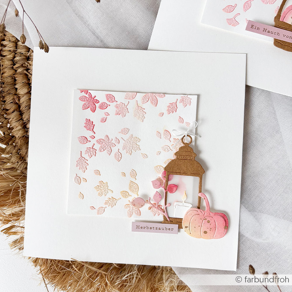 Handgefertigte Karte aus Designpapieren mit rosa und goldenen Blättern, einer Laterne, zwei Kürbissen, die mit dem Motivstanze-Kürbis-Stanzsystem hergestellt wurden, und einem Etikett mit der Aufschrift „Herbstzauber“.