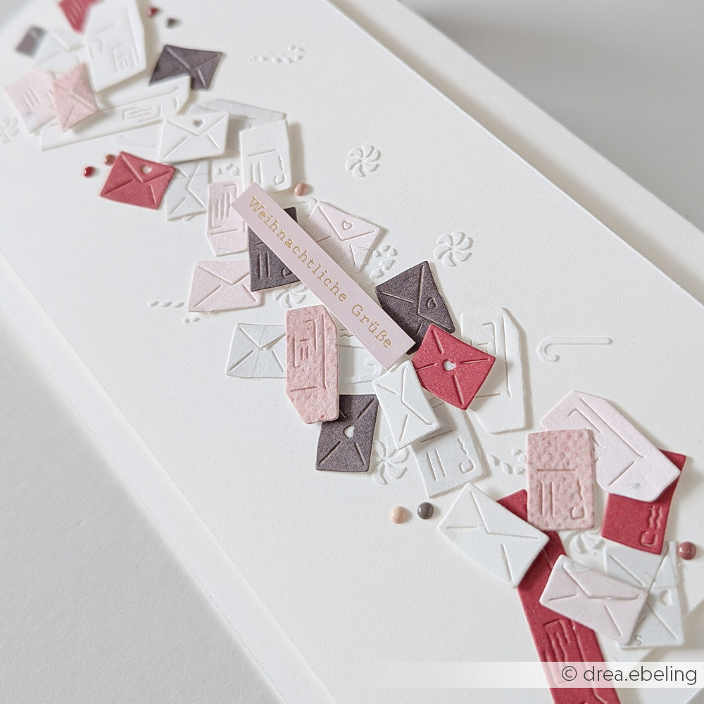 Weiße Karte mit geprägten Designpapieren und einem diagonalen Streifen aus Umschlägen mit der Aufschrift Weihnachtliche Grüße.