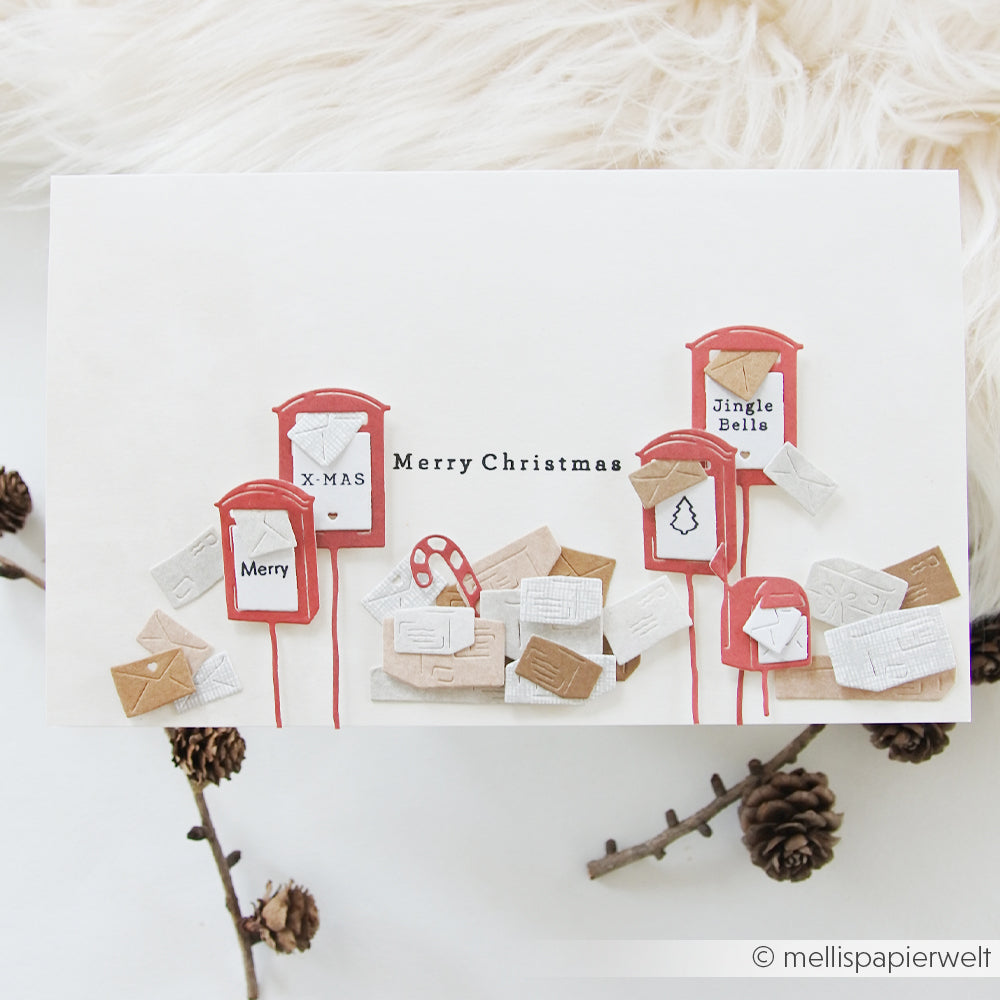 Eine Weihnachtskarte mit einem „Motivstanze Briefkasten Trio“ aus roten Briefkästen und verstreuten Briefumschlägen sowie dem Text „Merry Christmas“.