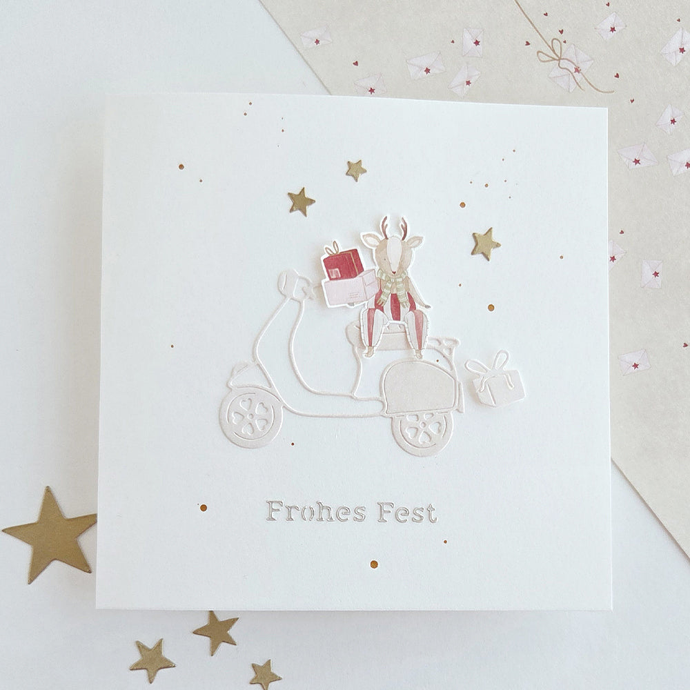 Eine Grußkarte mit einem Motiv aus der „Herzlicher Geschenke“-Reihe, das ein Rentier auf einem Roller mit Geschenken zeigt, versehen mit der Aufschrift „Frohes Fest“.