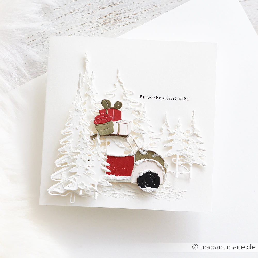 Ein kleines Auto, das Geschenke durch einen verschneiten Wald transportiert, gefertigt aus Designpapieren von DieCut Systeme.