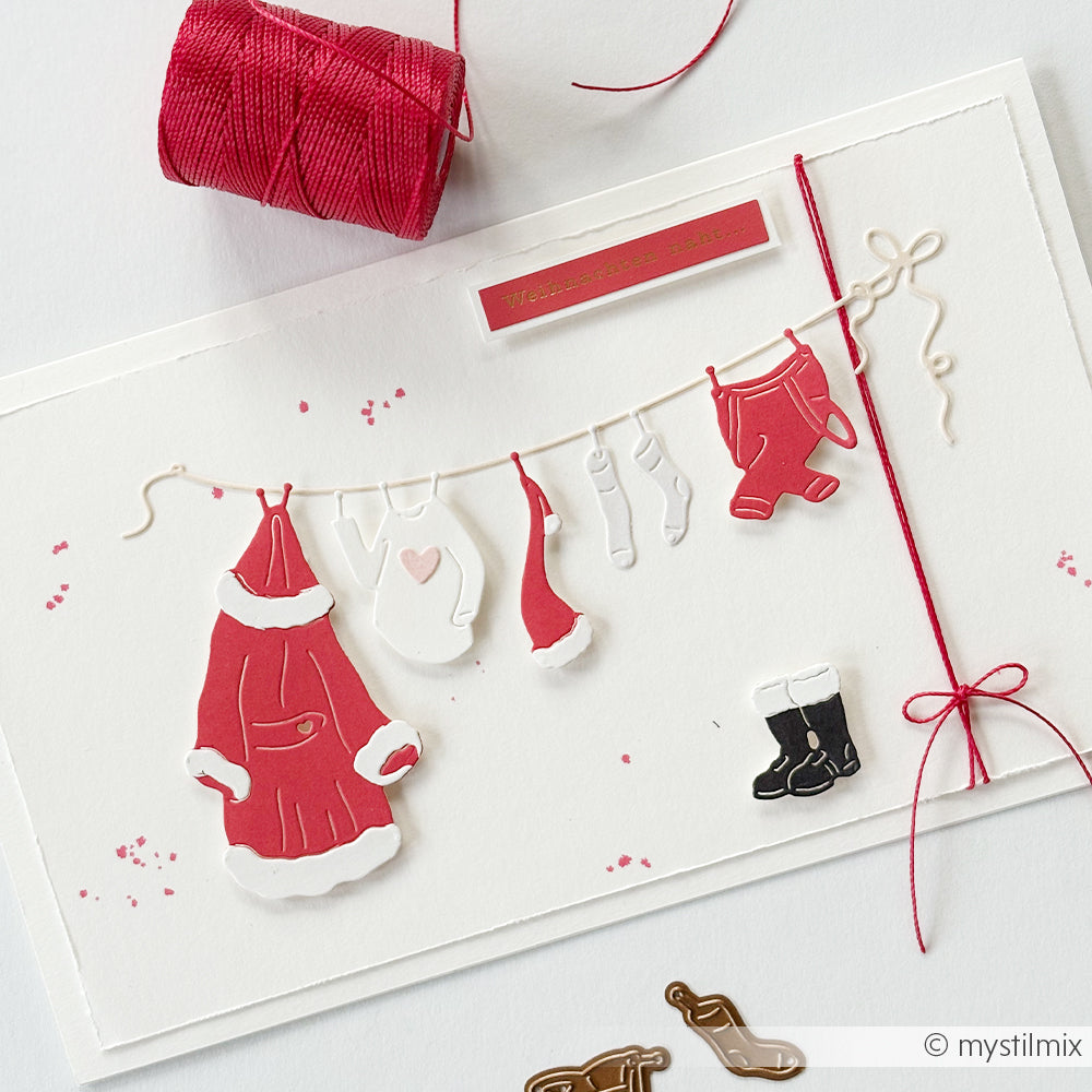 Eine handgefertigte Weihnachtskarte mit ausgestanzten Weihnachtsmann-Kleidungsstücken, die mit der Motivstanze „Santas Wäscheleine“ hergestellt wurden und an einer Wäscheleine aus Schnur hängen.