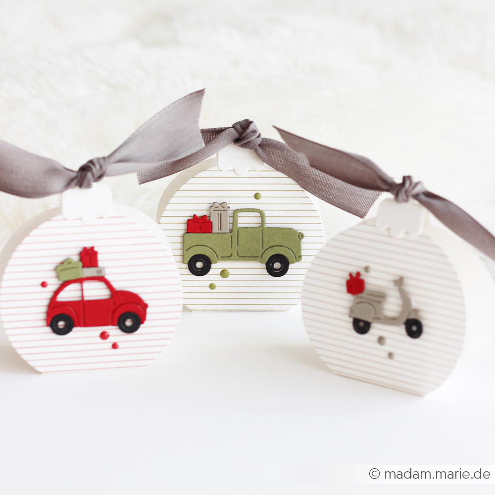 Drei runde Geschenkboxen mit grauen Bändern, verziert mit Papiermotiven von Motivstanze Geschenkefahrt.