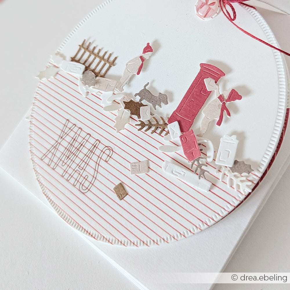 Eine runde Karte mit weihnachtlichen Papierausschnitten und Motivstanze-Motiven wie einem Briefkasten, einem Hund und XMAS.