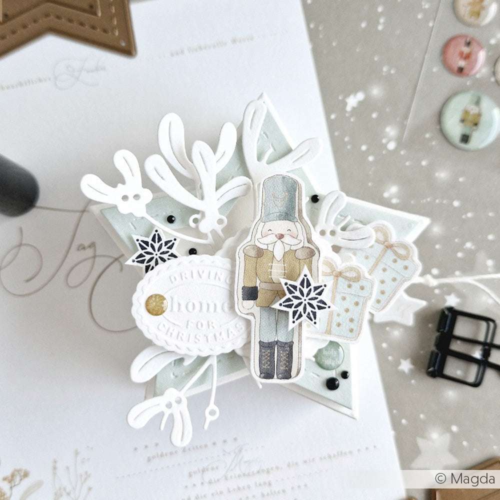 Handgefertigte Weihnachtskarte von Alexandra Renke mit einem Nussknacker, Geschenken, Schneeflocken und festlichen Dekorationen auf einem sternförmigen Sockel, mit einzigartigen Akzent-Stempel- und Holzstempel-Details für ein charmantes Finish.