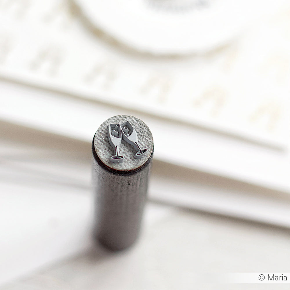 Ein Akzent-Stempel aus Metall von Alexandra Renke, auf dem zwei Sektgläser eingraviert sind - ideal, um einen festlichen Akzent in Ihrem Handwerk zu setzen.