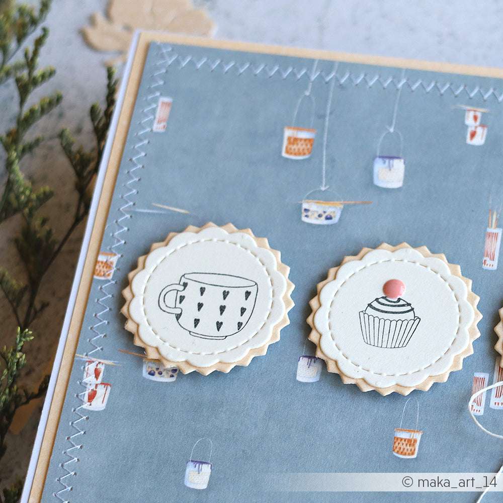 Handgefertigte Karte mit gezackten Kreisen, die eine Tasse und einen Cupcake auf einem blau gemusterten Hintergrund zeigen, gestempelt mit dem Alexandra Renke Herzchentasse Design.