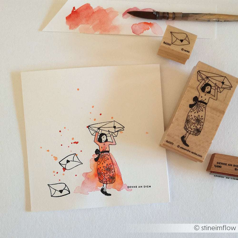 Ein handgezeichnetes Alexandra Renke Briefe-Figurinen Kind hält einen Papierschiffchen-Hut, umgeben von Briefumschlägen, Aquarellmaterial und charmanten Holzstempel-Stempelmotiven.