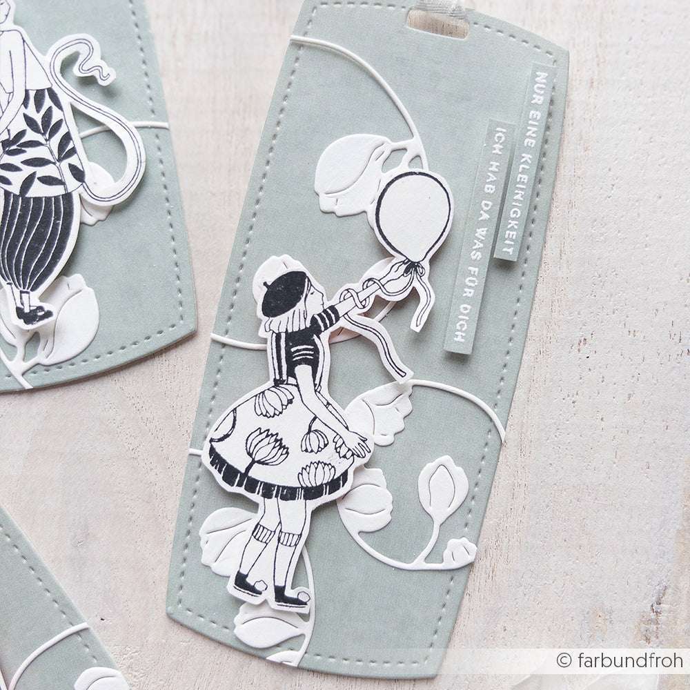 Papierausschnitt von einem Kind mit Luftballon auf einem dekorativen Anhänger mit Blumenmuster, deutschem Text und Akzenten mit Stempelgummi von Alexandra Renke.