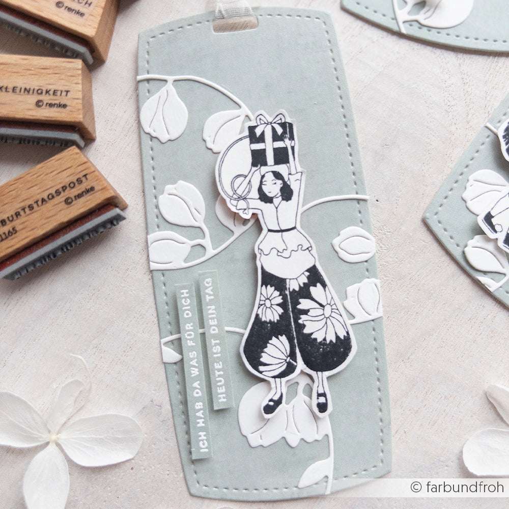 Lesezeichen mit einem ausgeschnittenen Mädchen mit Geschenk, Blumenmustern und deutschem Text auf hellgrau - perfekt für Papierprojekte. Hergestellt mit dem Alexandra Renke Holzstempel "Kind mit Geschenk".