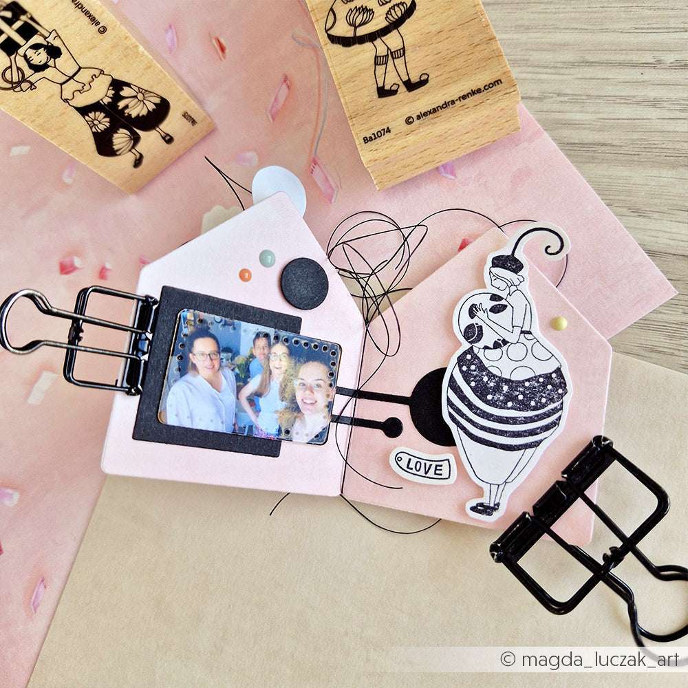 Das handgefertigte Scrapbook von Alexandra Renke zeigt ein Familienfoto, dekorative Ausschnitte, schwarze Heftklammern und charmante Holzstempel-Akzente auf einem rosa Hintergrund.