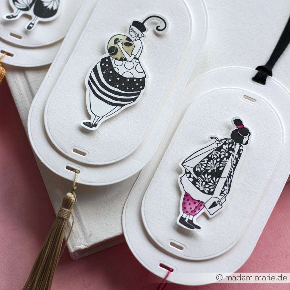 Die drei eleganten ovalen Lesezeichen von Alexandra Renke sind mit skurrilen Modeillustrationen und Quasten versehen. Jedes Design ist von Figurinen Kind mit Teebeutel inspiriert - und versprüht den Charme zarter Kunst, die an einen feinen Holzstempel erinnert.