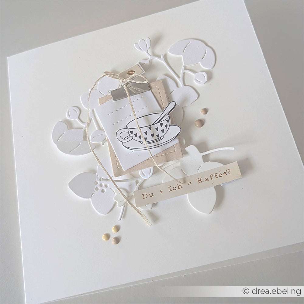 Diese handgefertigte Karte von Alexandra Renke zeigt eine Teetassen-Zeichnung, weiße Blumenausschnitte und ein "Du + Ich = Kaffee?"-Label. Die detaillierten Motive sind elegant mit hochwertigem Holz akzentuiert und sorgen für einen raffinierten Look.