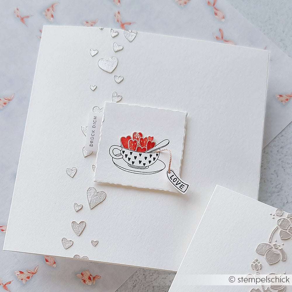 Handgemachte Karte auf weißem Papier mit einer Teetasse voller Erdbeeren, Herzmotiven und einem LOVE-Anhänger. Gestaltet mit Alexandra Renke Stempeln für gestochen scharfe Details.