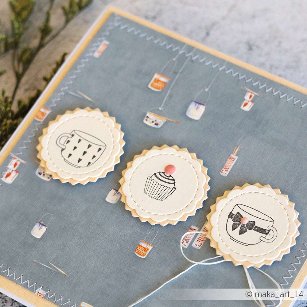 Die handgefertigte Karte von Alexandra Renke zeigt drei cremefarbene Kreise mit Tassen-, Cupcake- und Teetassenmotiven auf blauem Hintergrund - perfekt für Fans kreativer Holzstempel-Akzente.