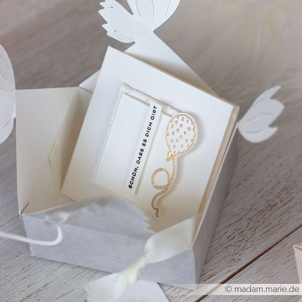 Weiße Alexandra Renke Geschenkbox mit Karte, die einen goldenen Luftballon und den Text "Schön, dass es dich gibt" zeigt - ideal für kreative Papierprojekte oder zur Kombination mit Ihren Lieblingsholzstempeln und Stempelmotiven.