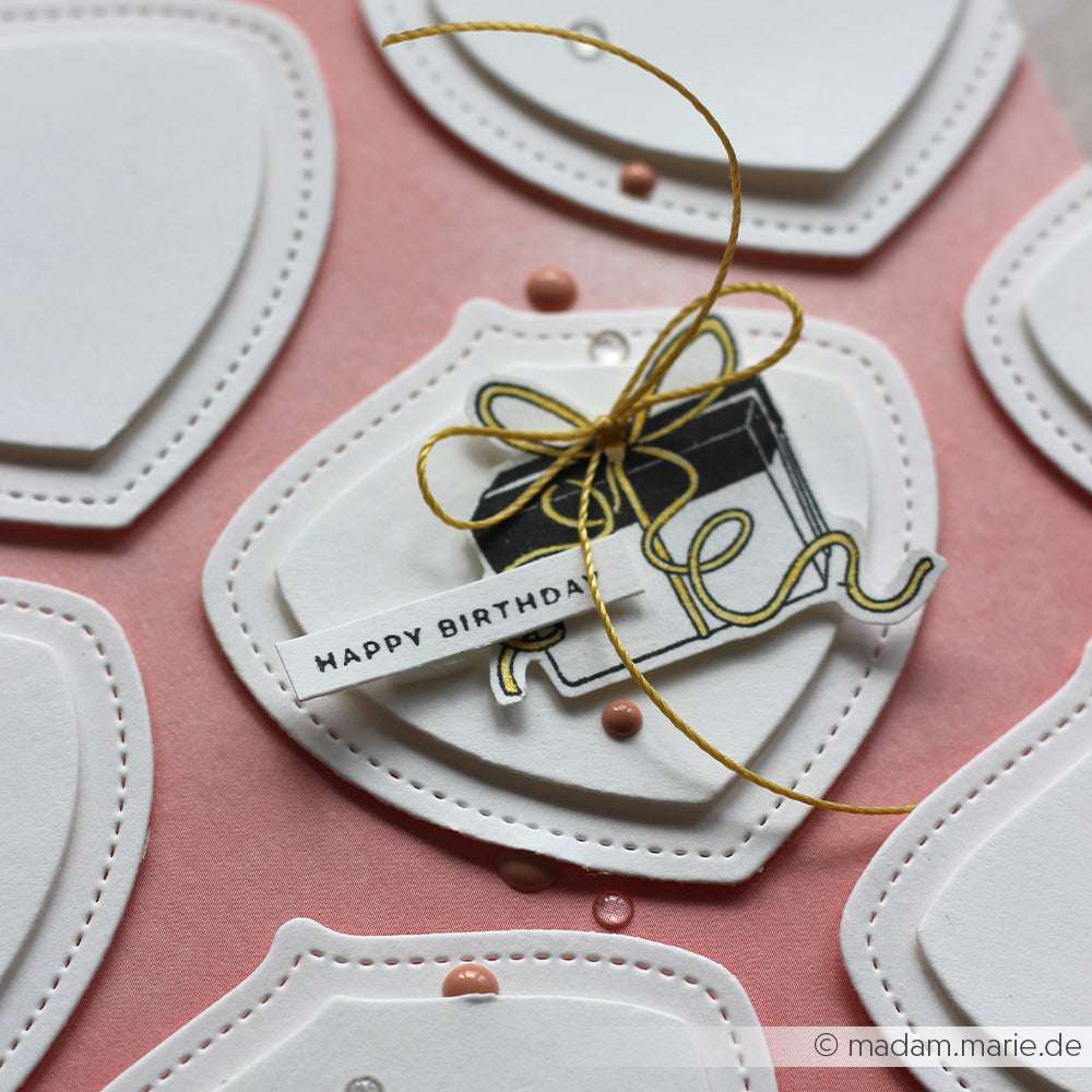 Geburtstagskarte von Alexandra Renke mit geschichteten weißen Formen, einer Geschenkzeichnung, goldener Schnur und einem Happy-Birthday-Anhänger auf rosa - wie ein Geschenk voller Freude, perfekt zu kombinieren mit Ihren Lieblings-Stempelkissen oder Holzstempeln.