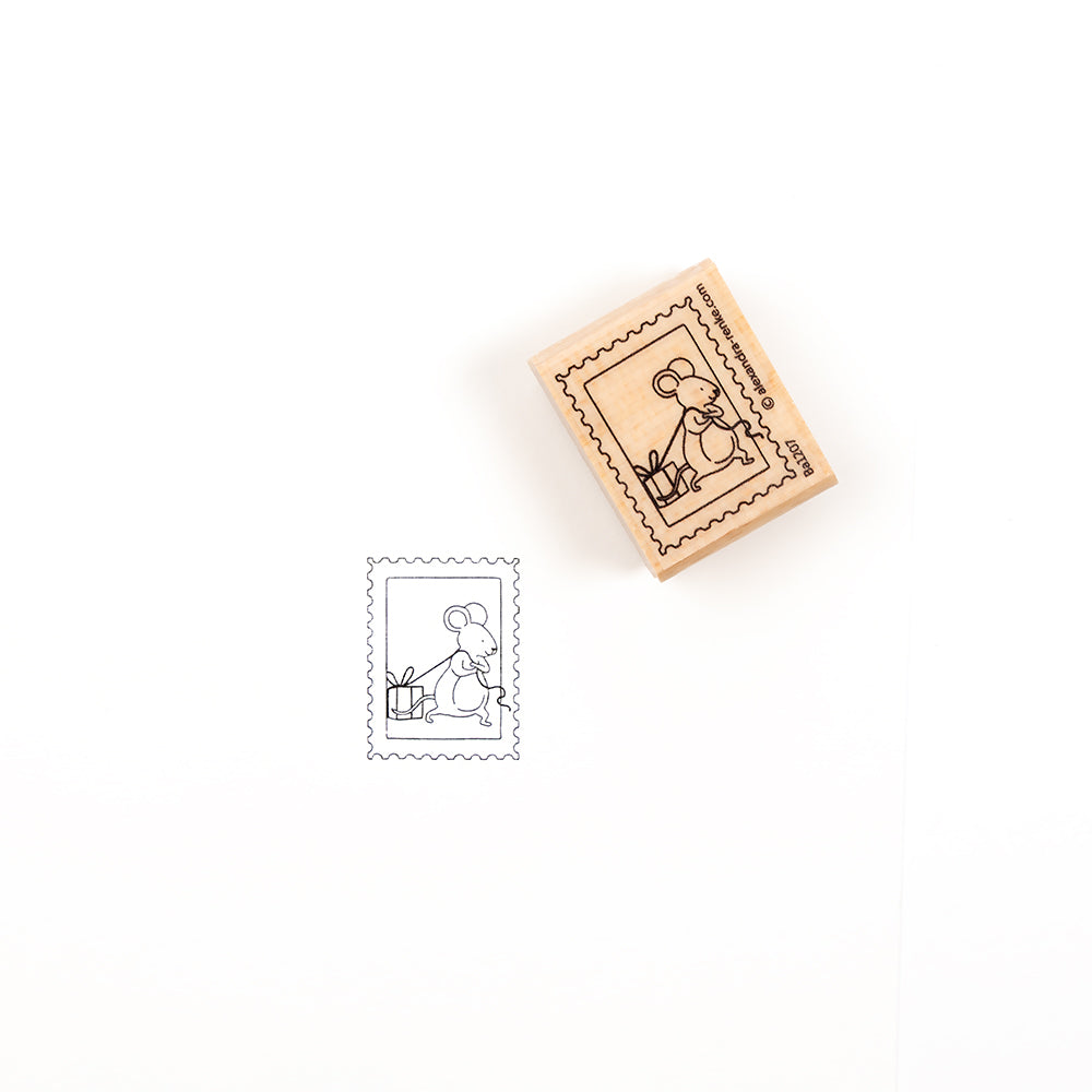 Ein Holzstempel, auf dem eine Maus zu sehen ist, die ein Geschenk hinter sich herzieht, daneben ein Abdruck des Motivs.