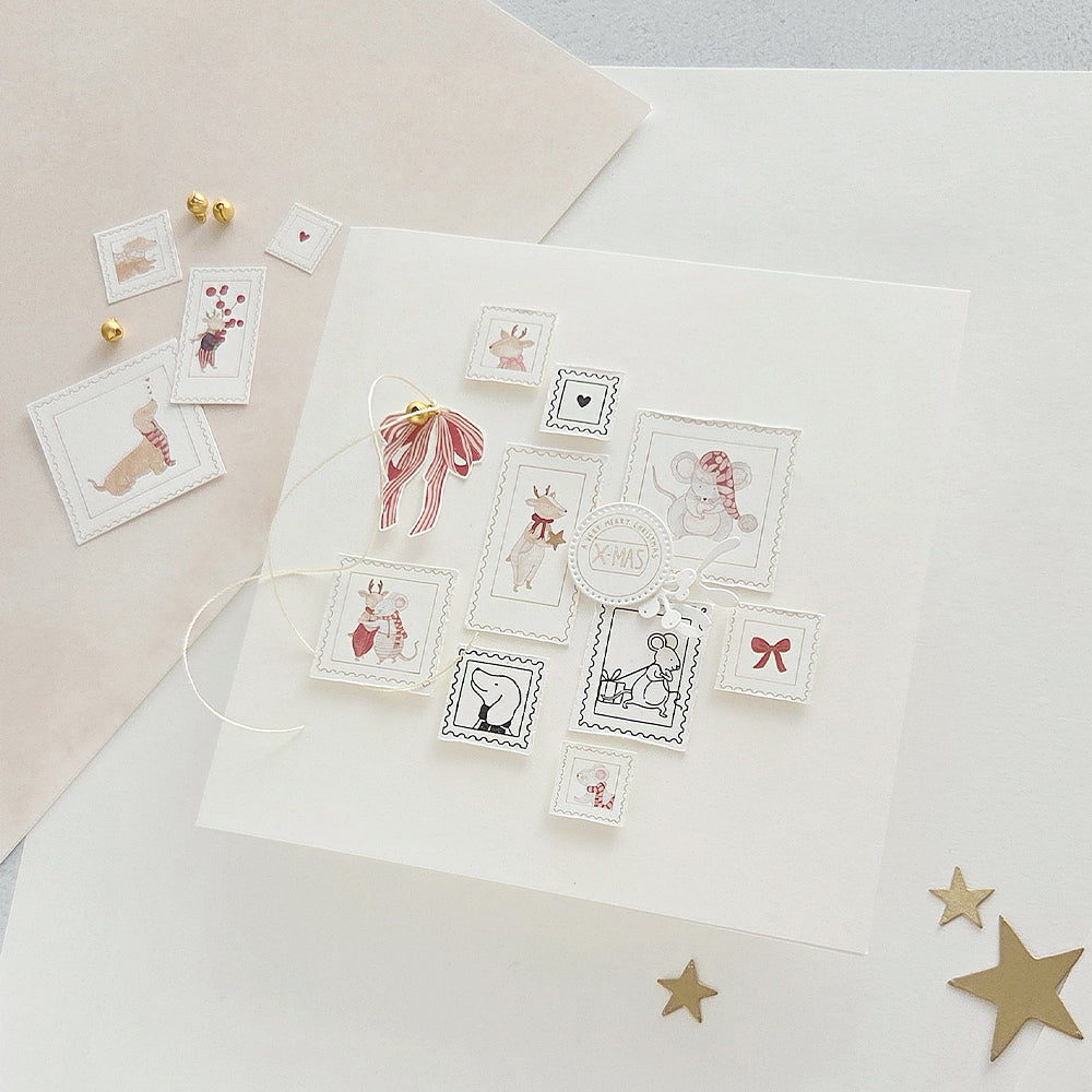 Eine weiße Karte, die mit mehreren illustrierten Weihnachtsbriefmarken verziert ist, die mit Holzstempeln aufgedruckt wurden.