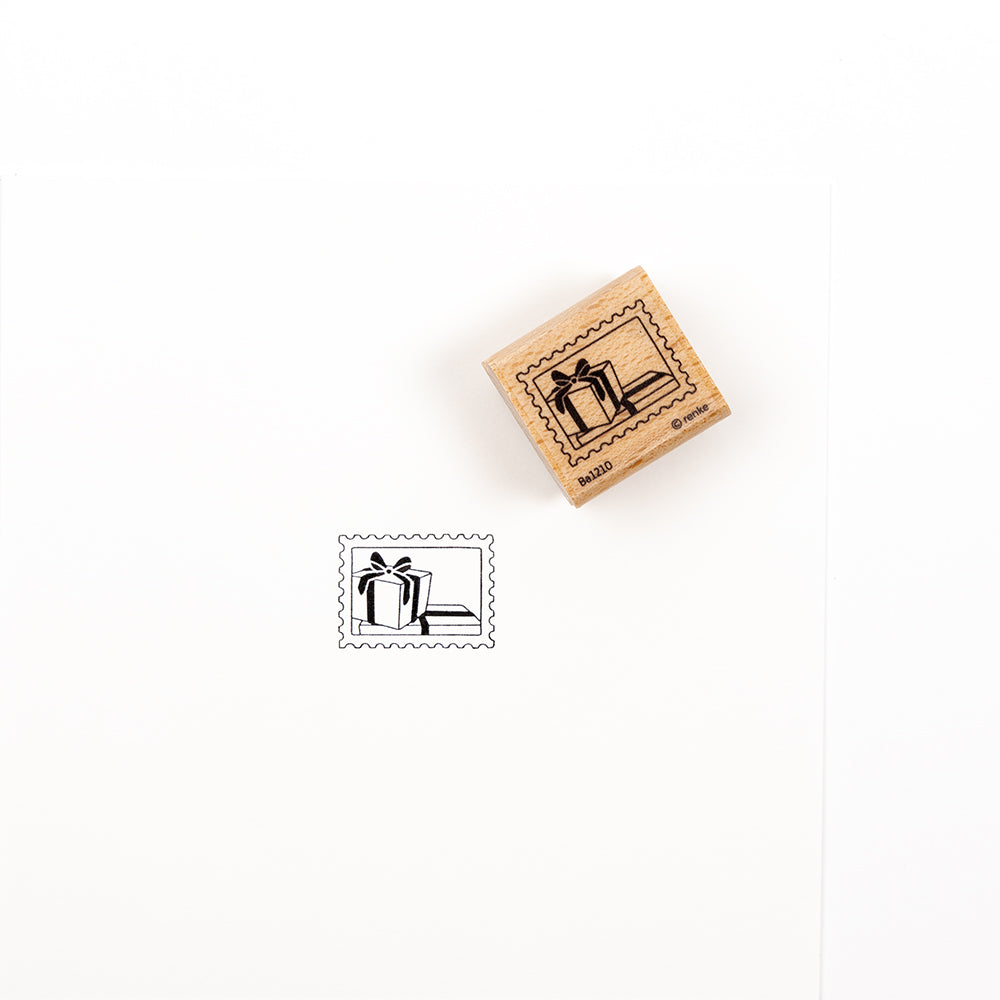Ein Holzstempel mit einem Geschenkbox-Motiv neben dem Stempelabdruck auf Papier.