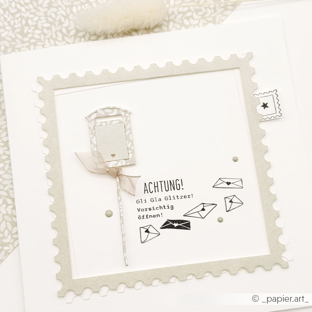 Handgefertigte Grußkarte mit einem Briefkasten, einem Sternstempel und dem deutschen Text Achtung! Gli Gla Glitzer!.