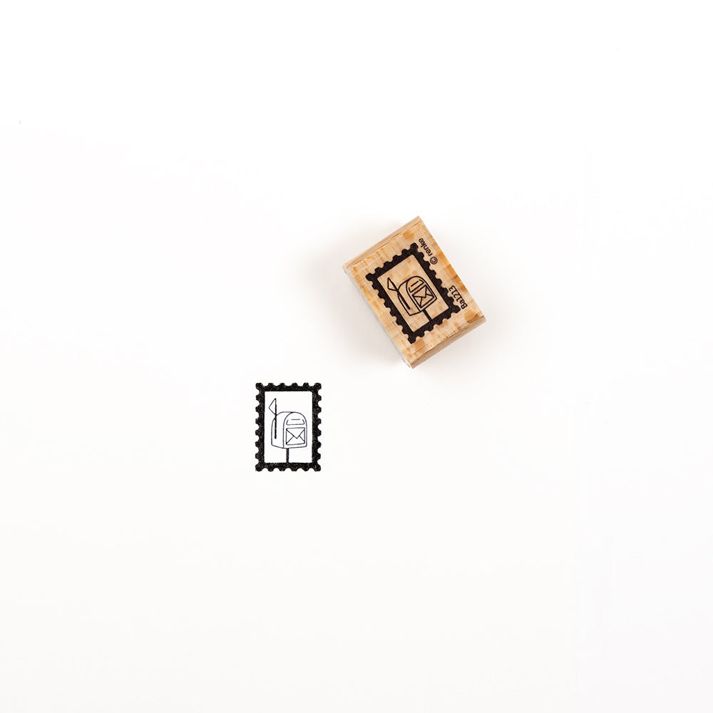 Ein Holzstempel und sein Stempelabdruck mit Postkastenmotiv, erstellt mit einem „Briefmarke Postkasten Holzstempel“.