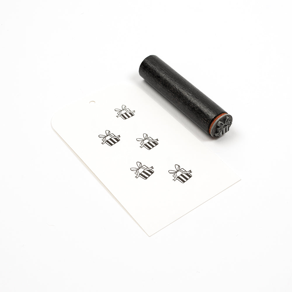 Ein Holzstempel und ein Anhänger, auf dem fünf kleine Geschenkbox-Symbole aufgedruckt sind.