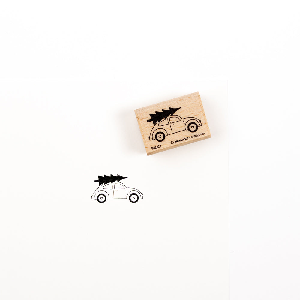 Ein Weihnachtsauto-Stempel aus Holz und sein Abdruck, der einen Oldtimer zeigt, auf dessen Dach ein Weihnachtsbaum thront.