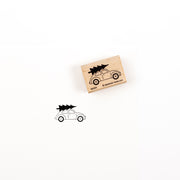 Ein Weihnachtsauto-Stempel aus Holz und sein Abdruck, der einen Oldtimer zeigt, auf dessen Dach ein Weihnachtsbaum thront.