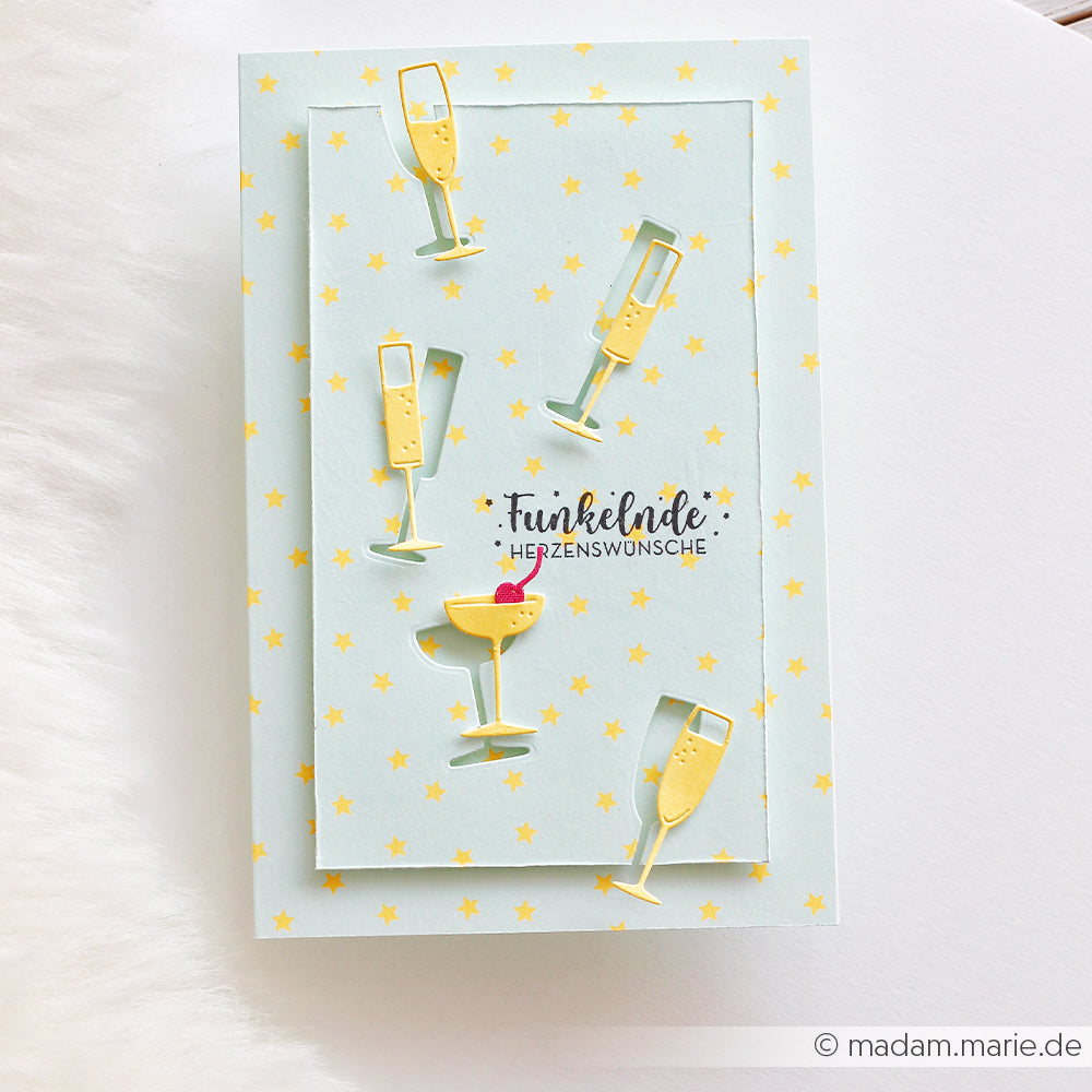 Grußkarte mit ausgeschnittenen Champagner- und Cocktailgläsern, gelben „Sommer Special Sterne“ und deutschem Text auf „Neon Papier“-Designpapier, alles vor einem hellblauen Hintergrund.