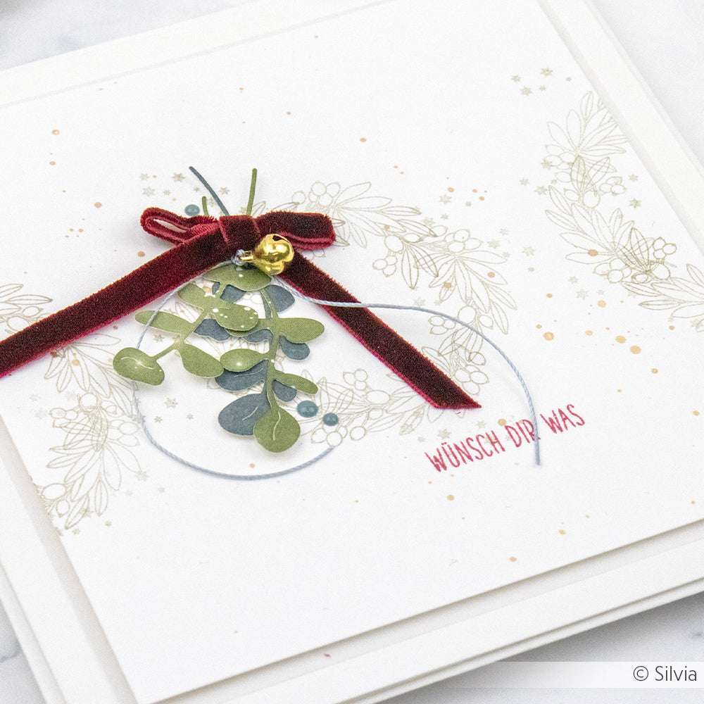 Handgefertigte Karte von Vivant Decorations BV mit einem blattförmigen Ornament, einer roten Samtschleife aus Florband und dem Text "Wünsch Dir Was" auf einem floralen Hintergrund.