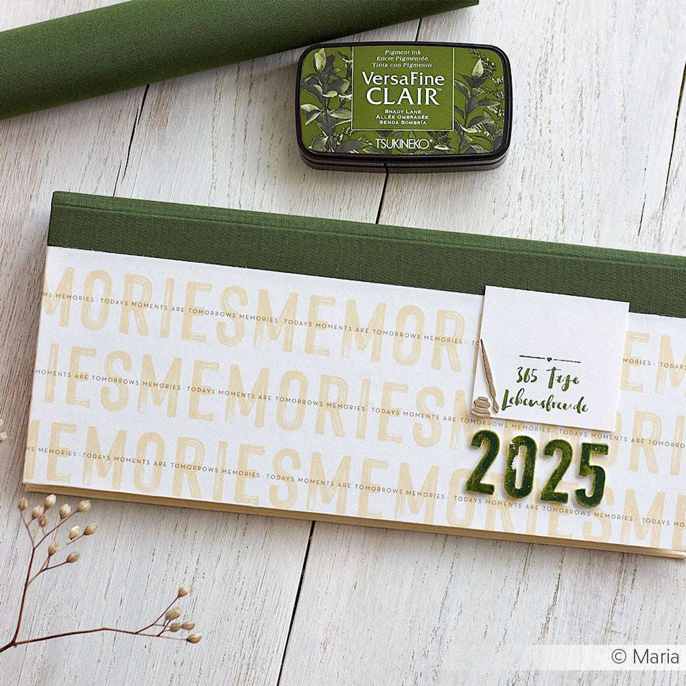 ☆ 2025 Tischkalender mit grünem Buchleineneinband, Stempelkissen und dekorativem Zweig auf einer Holzfläche.