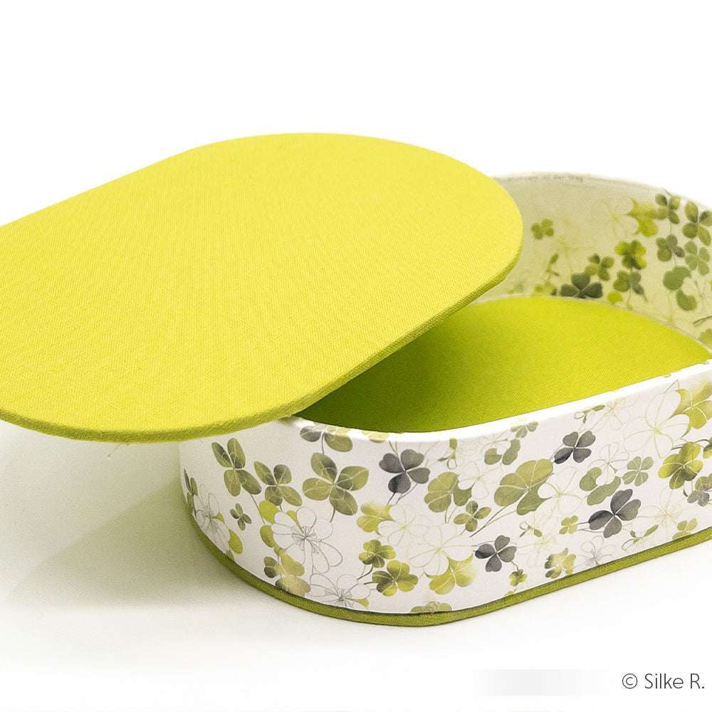 Ovale Dose von ☆ mit grünem Deckel, mit Kleeblattmuster in Buchleinen Viskose. Der Deckel ist teilweise geöffnet.