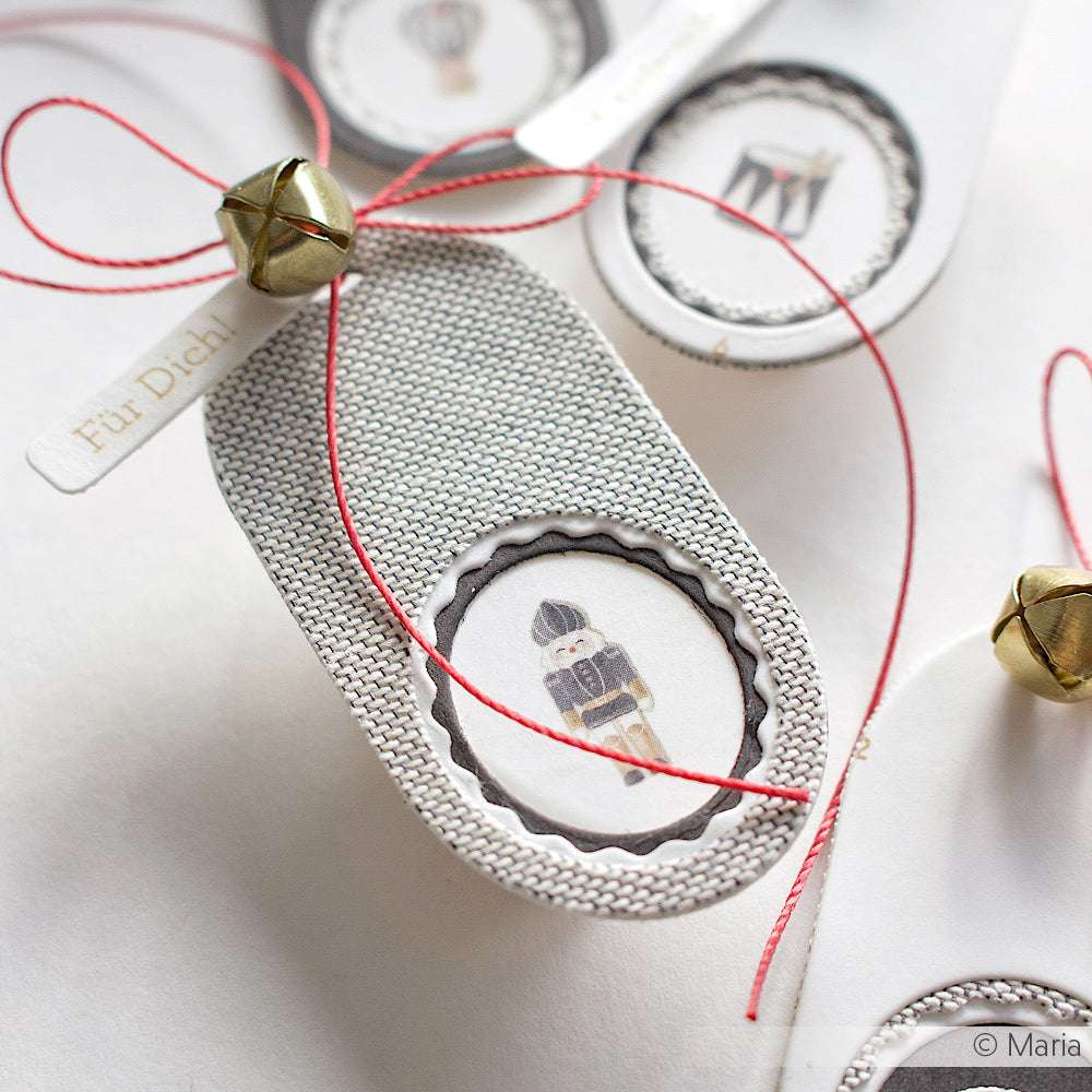 ☆ silberner Geschenkanhänger mit Nussknacker-Motiv, roter Schnur aus 100 % Baumwolle und einer kleinen goldenen Jingle Bell.