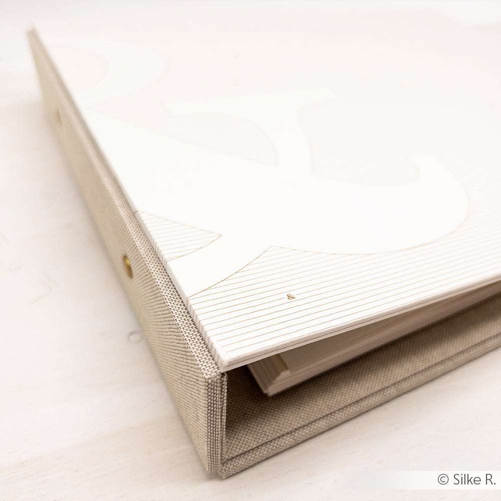 Ein beige-weißer, stoffbezogener Binder von ☆, hergestellt aus Buchleinen aus 100% Baumwolle, ruht auf einer hellen Fläche.
