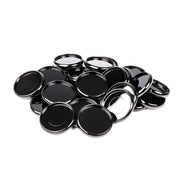 Ein Stapel glänzender, schwarzer Alexandra-Renke-Deckel mit silbernem Rand - ähnlich wie Bindescheiben - liegt auf einem weißen Hintergrund.