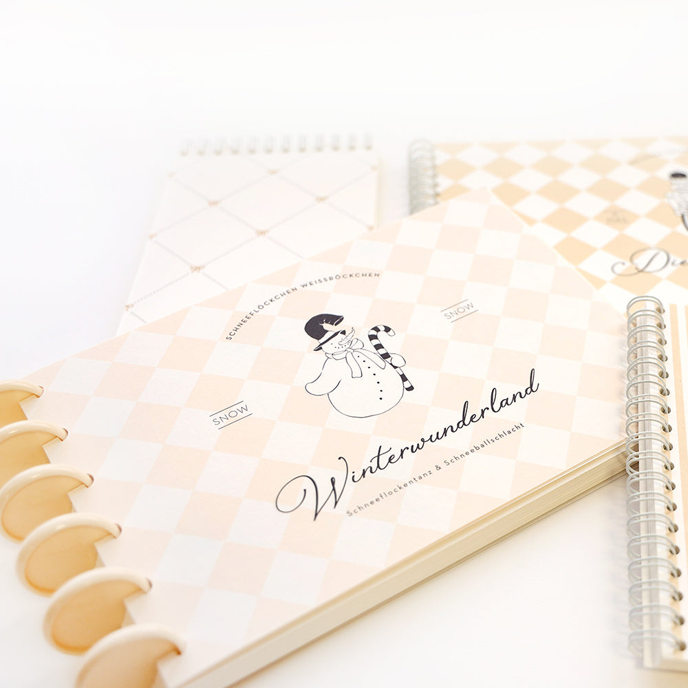 Die creme-weiß karierten Notizbücher von Alexandra Renke mit Schneemann-Illustration und "Winterwunderland" auf dem Cover sind mit Bindescheiben ausgestattet, die das Binden erleichtern.