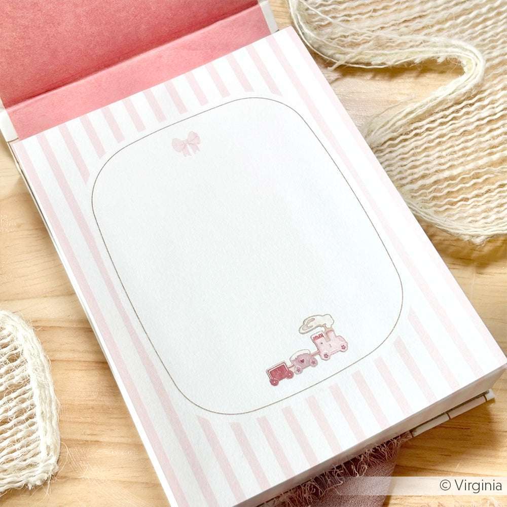 Der Alexandra Renke Notizblock mit rosa Streifen zeigt eine kleine rosa Spielzeugeisenbahn am unteren Rand jeder Seite. Gedruckt auf hochwertigem 100 g/m² Papier ist er perfekt für Notizen oder kreative Ideen.